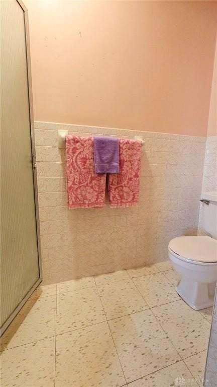 bathroom with toilet, tile patterned flooring, and tile walls