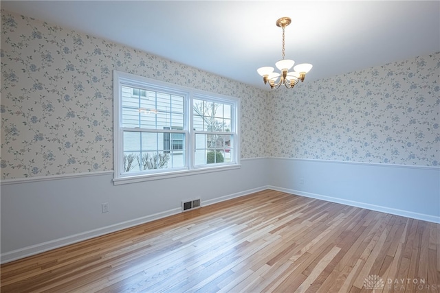 spare room with a chandelier and light wood-type flooring