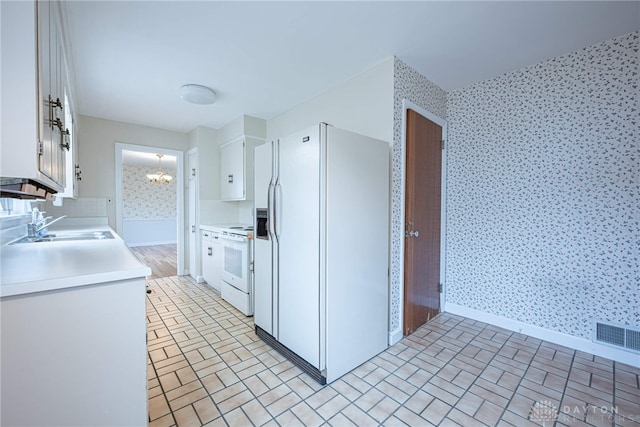 kitchen with sink, white appliances, a notable chandelier, and white cabinets