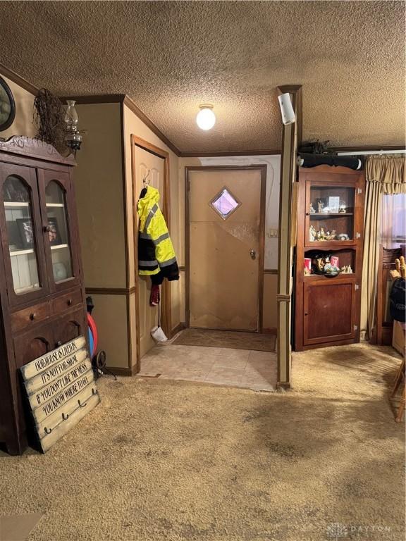 entryway with ornamental molding, light colored carpet, and a textured ceiling