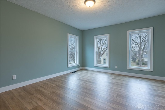 unfurnished room featuring a textured ceiling, light hardwood / wood-style flooring, and a wealth of natural light