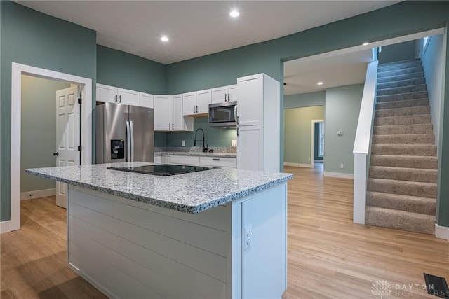 kitchen with stainless steel appliances, white cabinetry, light stone counters, and light hardwood / wood-style floors