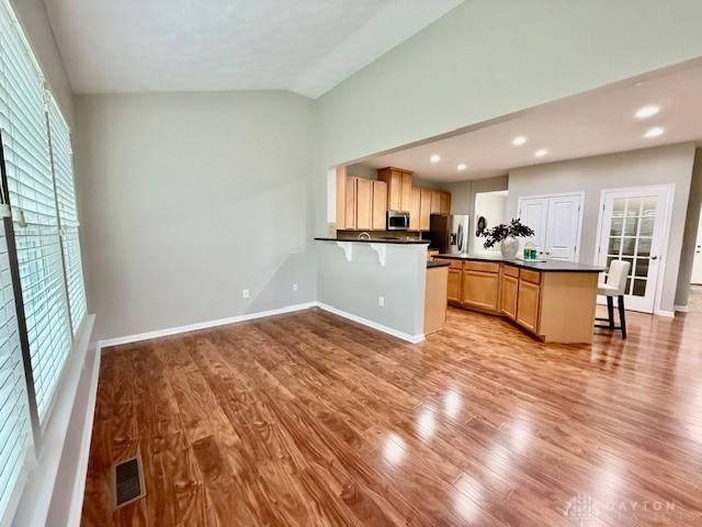 kitchen featuring vaulted ceiling, light hardwood / wood-style flooring, light brown cabinets, appliances with stainless steel finishes, and kitchen peninsula