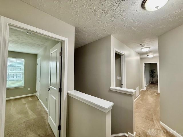 corridor with light colored carpet and a textured ceiling