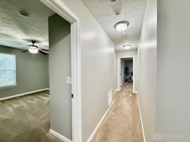 corridor with light colored carpet and a textured ceiling