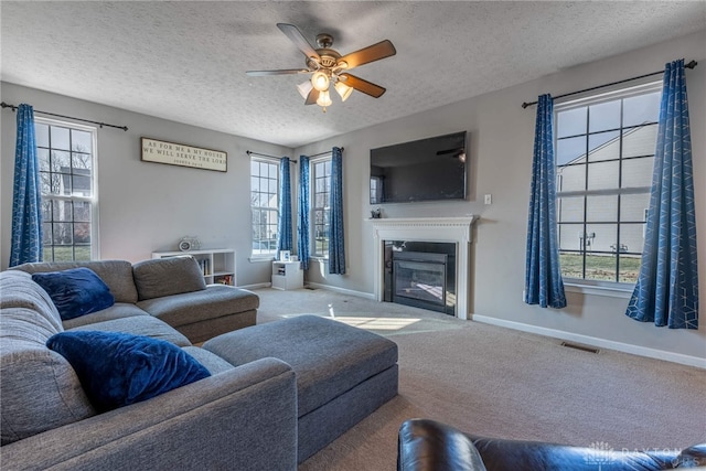 carpeted living area featuring baseboards, a wealth of natural light, and a glass covered fireplace