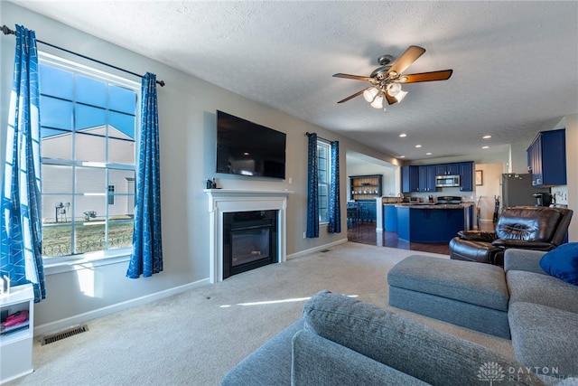 carpeted living room with a glass covered fireplace, visible vents, a textured ceiling, and baseboards