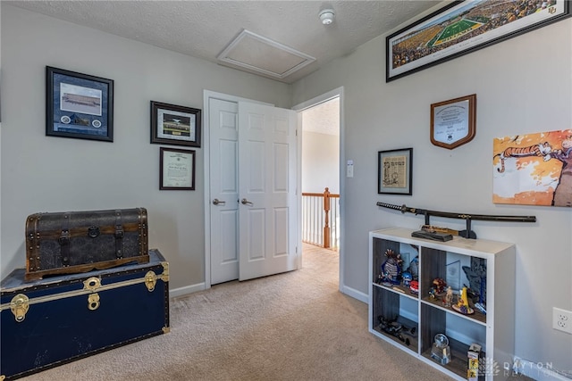 sitting room featuring attic access, light colored carpet, a textured ceiling, and baseboards