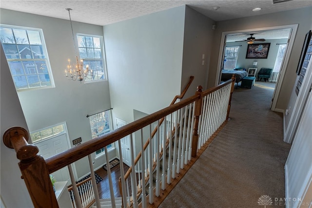 corridor with carpet floors, a chandelier, a textured ceiling, and an upstairs landing