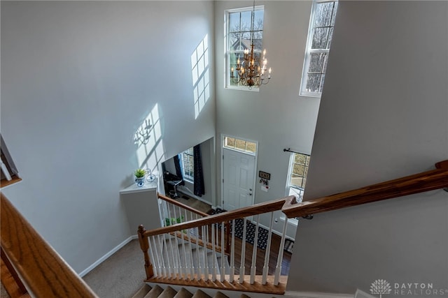 stairway with baseboards, a high ceiling, carpet flooring, and a notable chandelier