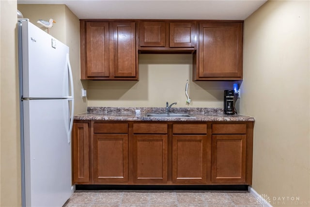 kitchen with brown cabinetry, a sink, and freestanding refrigerator