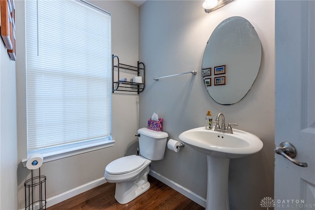 half bath featuring toilet, a sink, baseboards, and wood finished floors