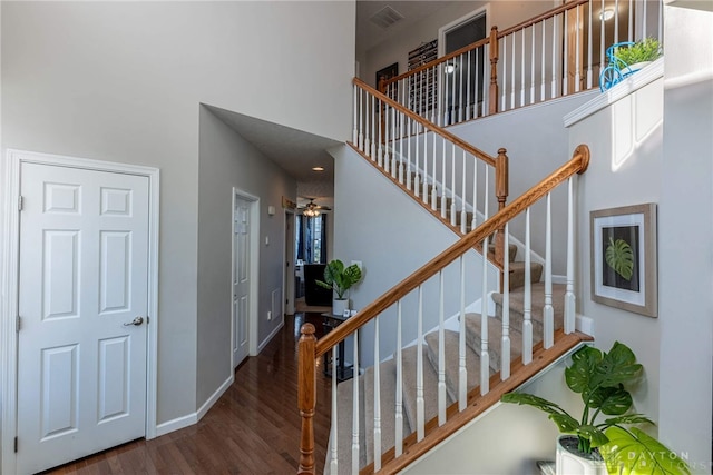 staircase with baseboards, visible vents, a high ceiling, and wood finished floors