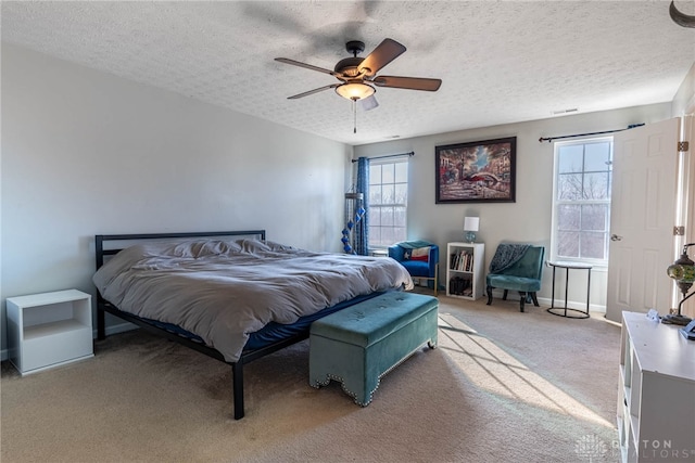 bedroom featuring light carpet, ceiling fan, baseboards, and a textured ceiling