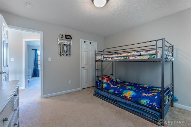 bedroom with light carpet, a textured ceiling, and baseboards