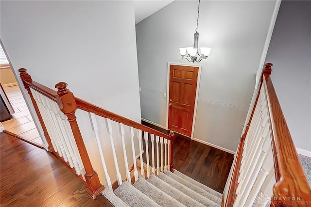 staircase with high vaulted ceiling, a notable chandelier, baseboards, and wood finished floors