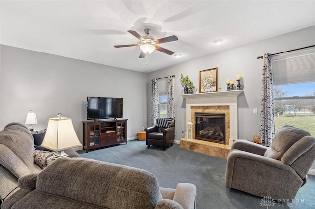 living room with a tile fireplace, dark colored carpet, and ceiling fan