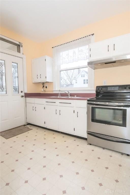 kitchen featuring stainless steel electric stove, sink, and white cabinets