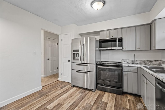 kitchen with gray cabinetry, hardwood / wood-style floors, sink, and appliances with stainless steel finishes