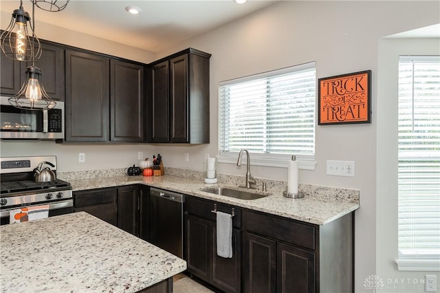 kitchen with stainless steel appliances, hanging light fixtures, sink, and light stone counters