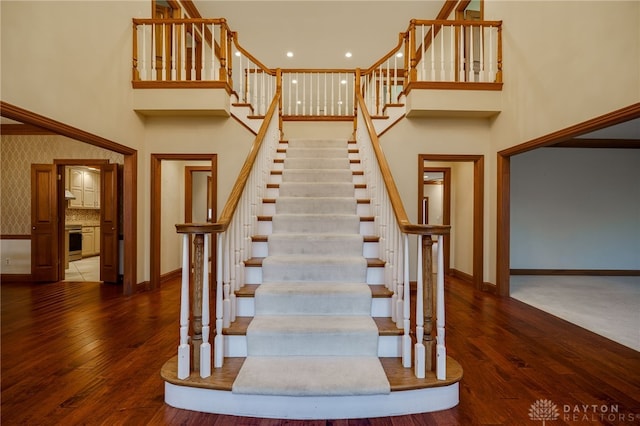 stairway featuring hardwood / wood-style floors, baseboards, and a high ceiling