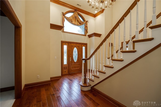 entryway with crown molding, wood-type flooring, an inviting chandelier, baseboards, and a high ceiling