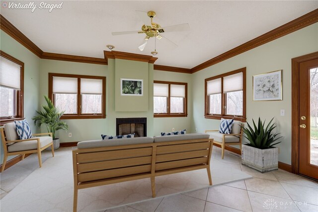 living area with a fireplace, ornamental molding, ceiling fan, and plenty of natural light