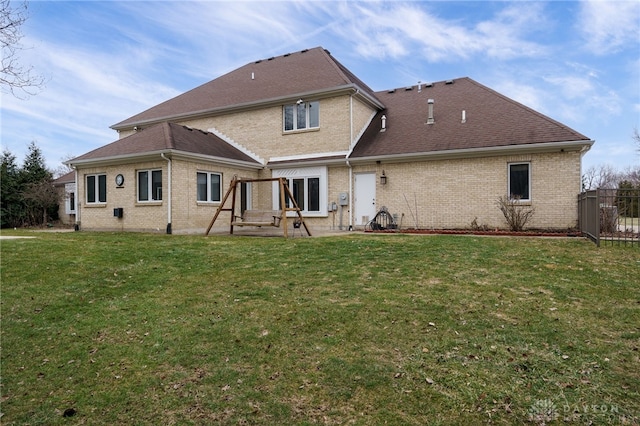 rear view of house featuring fence, a patio, roof with shingles, brick siding, and a lawn
