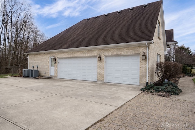 view of home's exterior featuring driveway, a shingled roof, brick siding, and central AC