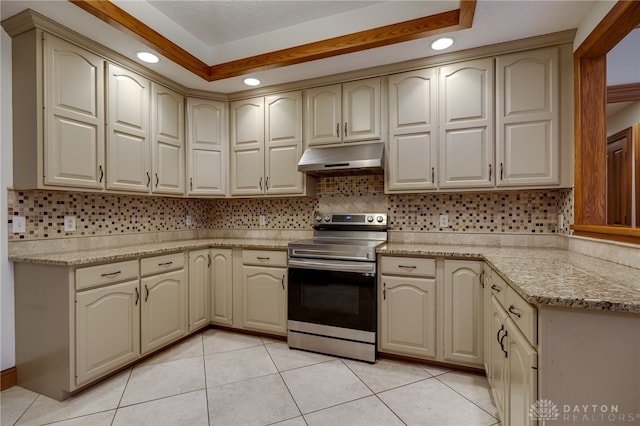 kitchen with light tile patterned flooring, under cabinet range hood, cream cabinets, stainless steel electric stove, and decorative backsplash