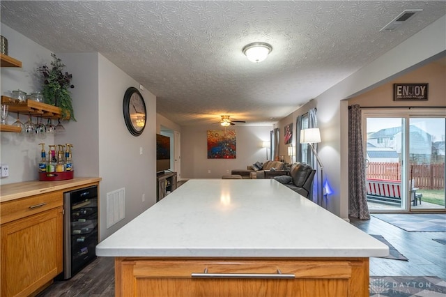 kitchen with wine cooler, a textured ceiling, dark hardwood / wood-style floors, a kitchen island, and ceiling fan