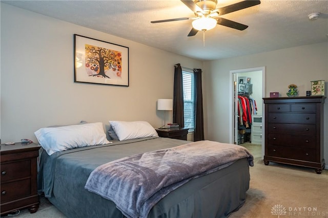 bedroom with a walk in closet, light colored carpet, ceiling fan, a textured ceiling, and a closet