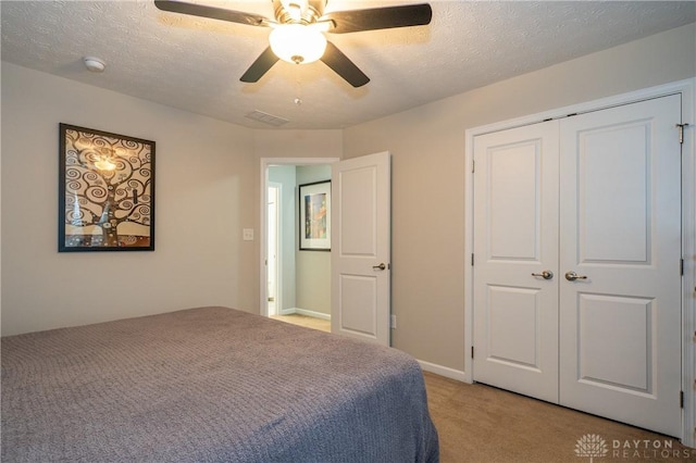 bedroom featuring ceiling fan, light carpet, a textured ceiling, and a closet