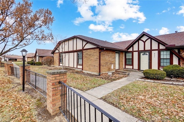 view of front facade with a shingled roof, brick siding, fence, and stucco siding