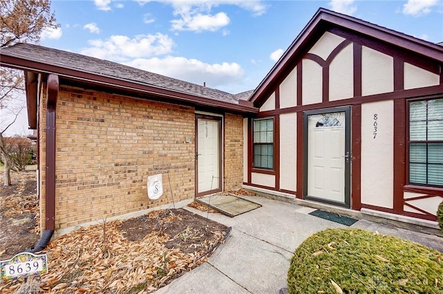 entrance to property featuring brick siding and roof with shingles