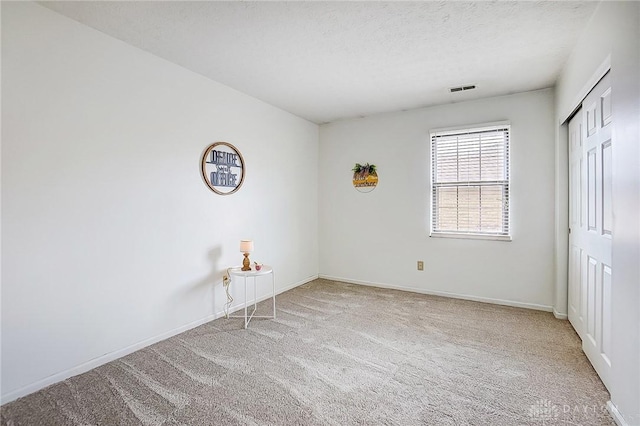 carpeted empty room featuring a textured ceiling, visible vents, and baseboards