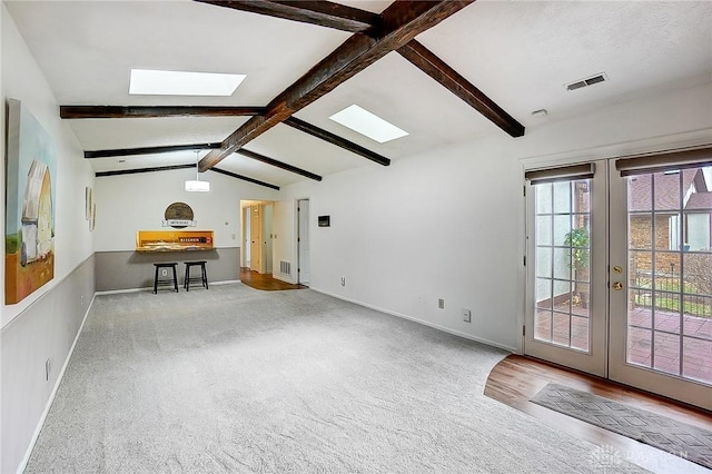 interior space featuring carpet, vaulted ceiling with skylight, visible vents, and french doors