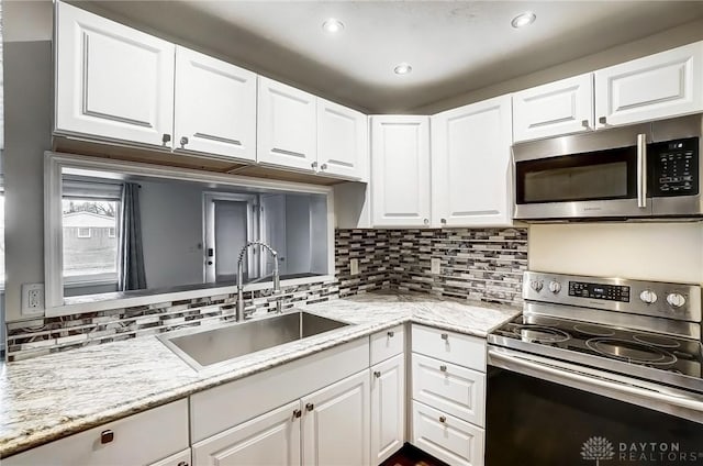 kitchen with sink, white cabinetry, appliances with stainless steel finishes, light stone countertops, and decorative backsplash