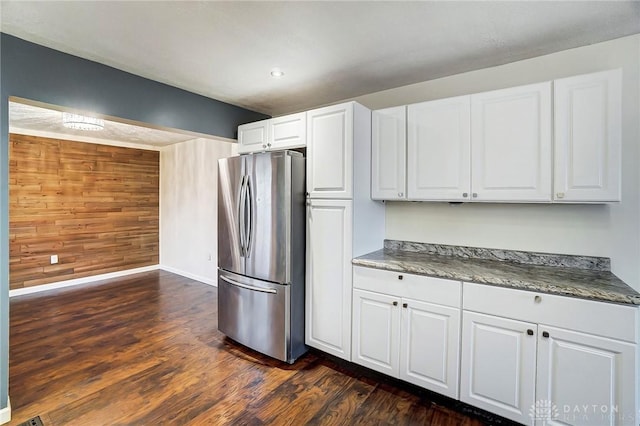 kitchen featuring stainless steel refrigerator, wooden walls, dark wood-type flooring, and white cabinets