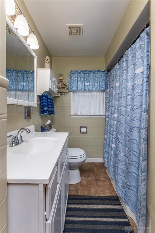 bathroom with tile patterned flooring, tile walls, vanity, curtained shower, and toilet