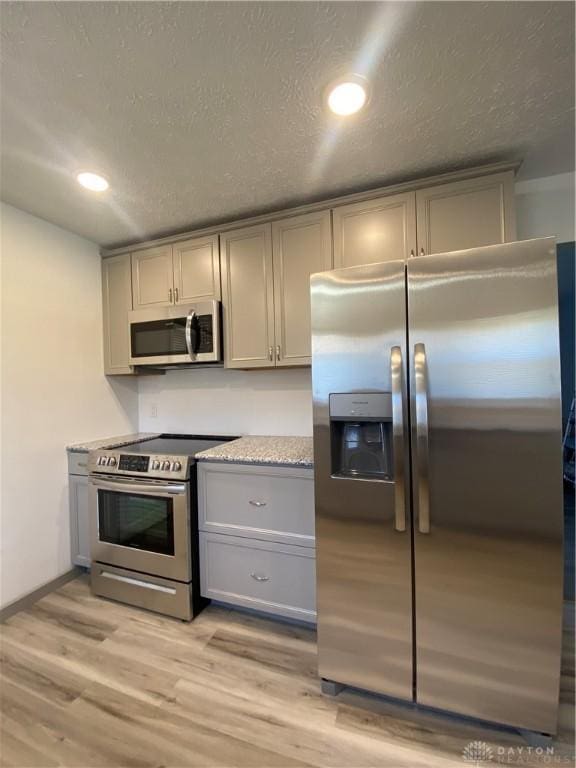 kitchen featuring gray cabinets, appliances with stainless steel finishes, a textured ceiling, and light wood-type flooring