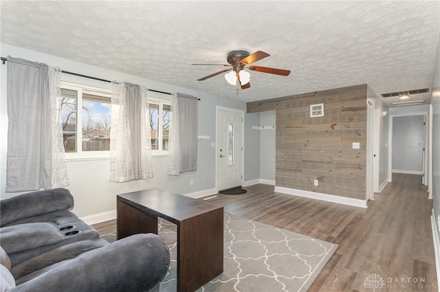 living room with ceiling fan, wood-type flooring, wooden walls, and a textured ceiling