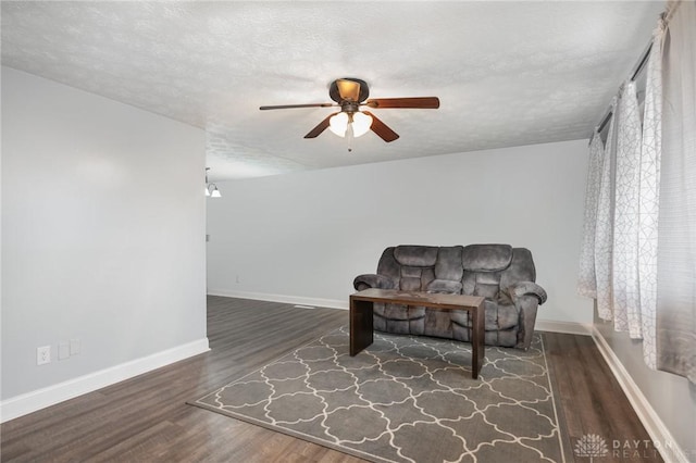 living area with ceiling fan, dark wood-type flooring, and a textured ceiling