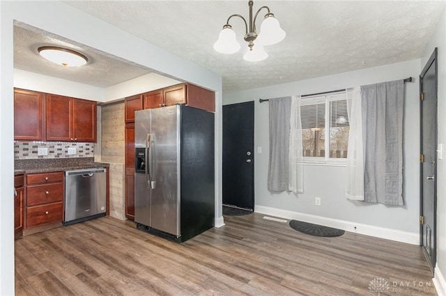 kitchen featuring pendant lighting, dark wood-type flooring, appliances with stainless steel finishes, a textured ceiling, and decorative backsplash