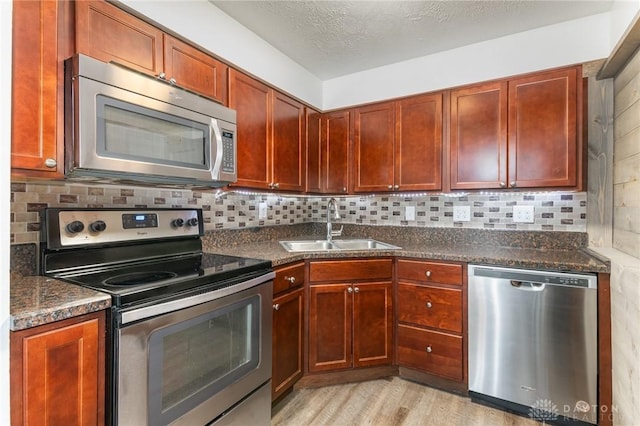 kitchen featuring sink, dark stone countertops, decorative backsplash, light hardwood / wood-style floors, and stainless steel appliances