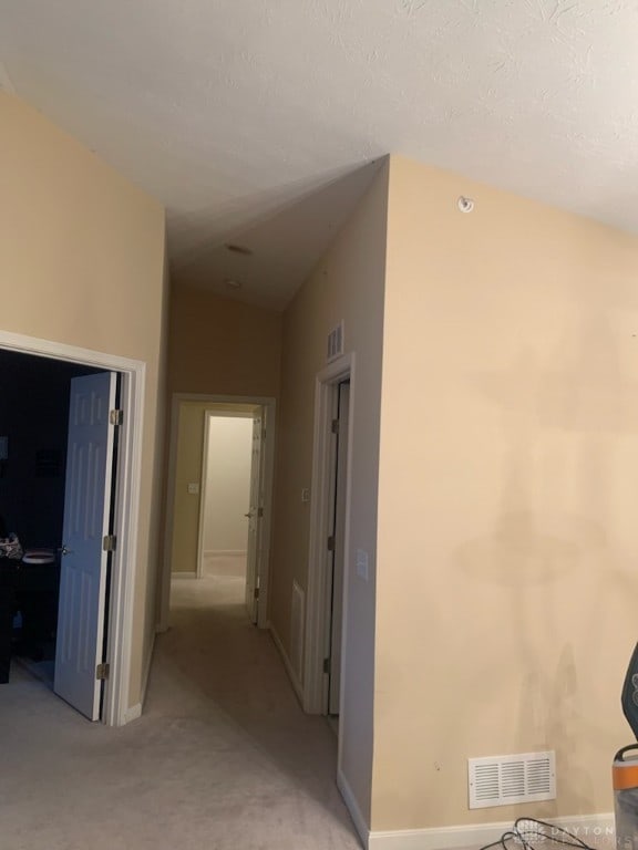 hallway featuring vaulted ceiling and light carpet