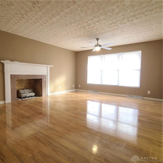 unfurnished living room with a tiled fireplace, ceiling fan, a textured ceiling, and light wood-type flooring