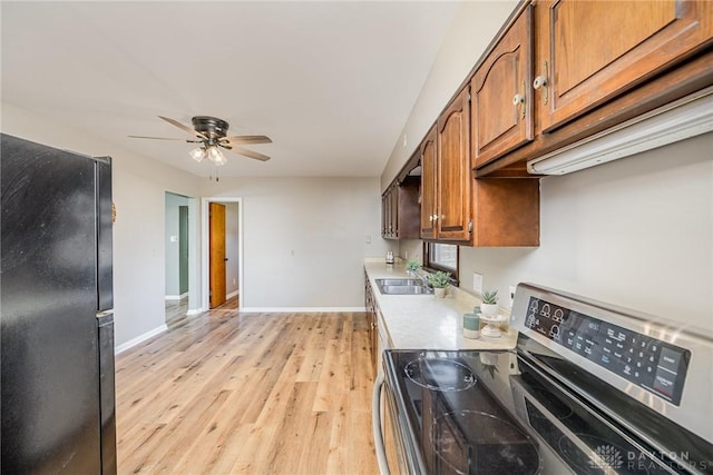 kitchen featuring brown cabinets, light countertops, freestanding refrigerator, stainless steel range with electric cooktop, and a sink