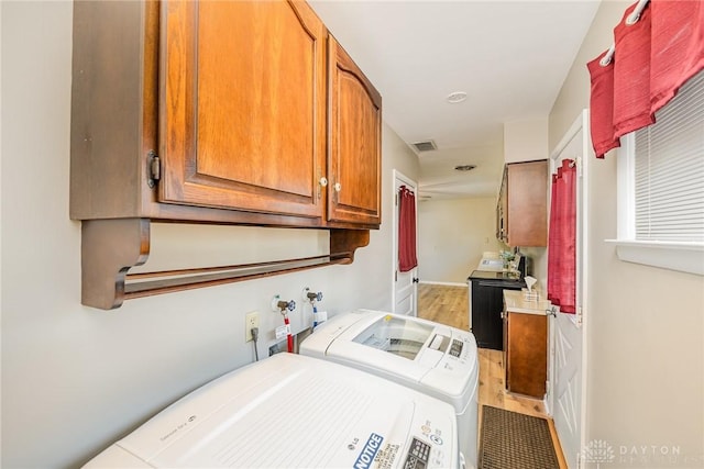 clothes washing area with visible vents, light wood finished floors, independent washer and dryer, and cabinet space