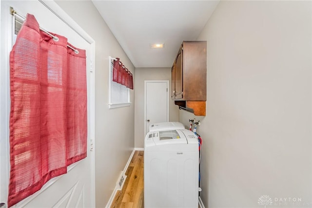 clothes washing area featuring washer / dryer, light wood-type flooring, cabinet space, and baseboards